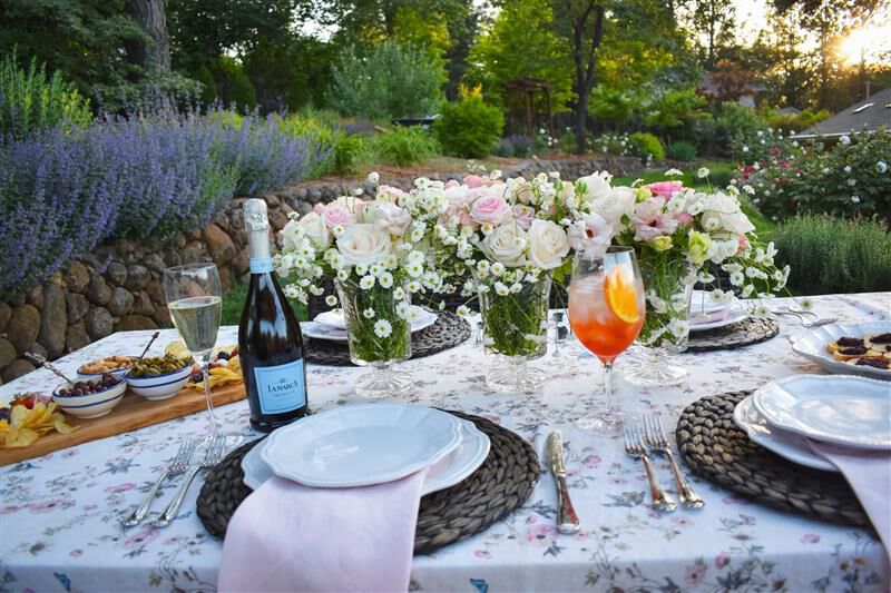 Elegant outdoor garden table set with floral arrangements, La Marca Prosecco, a spritz cocktail, and place settings for entertaining.