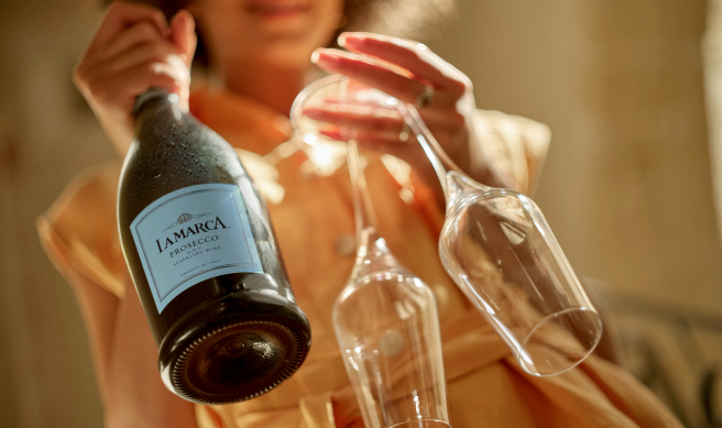 A bottle of La Marca Prosecco featuring the signature light blue label and silver foil top, showcasing the delicate pink hue of the sparkling wine through the clear glass.