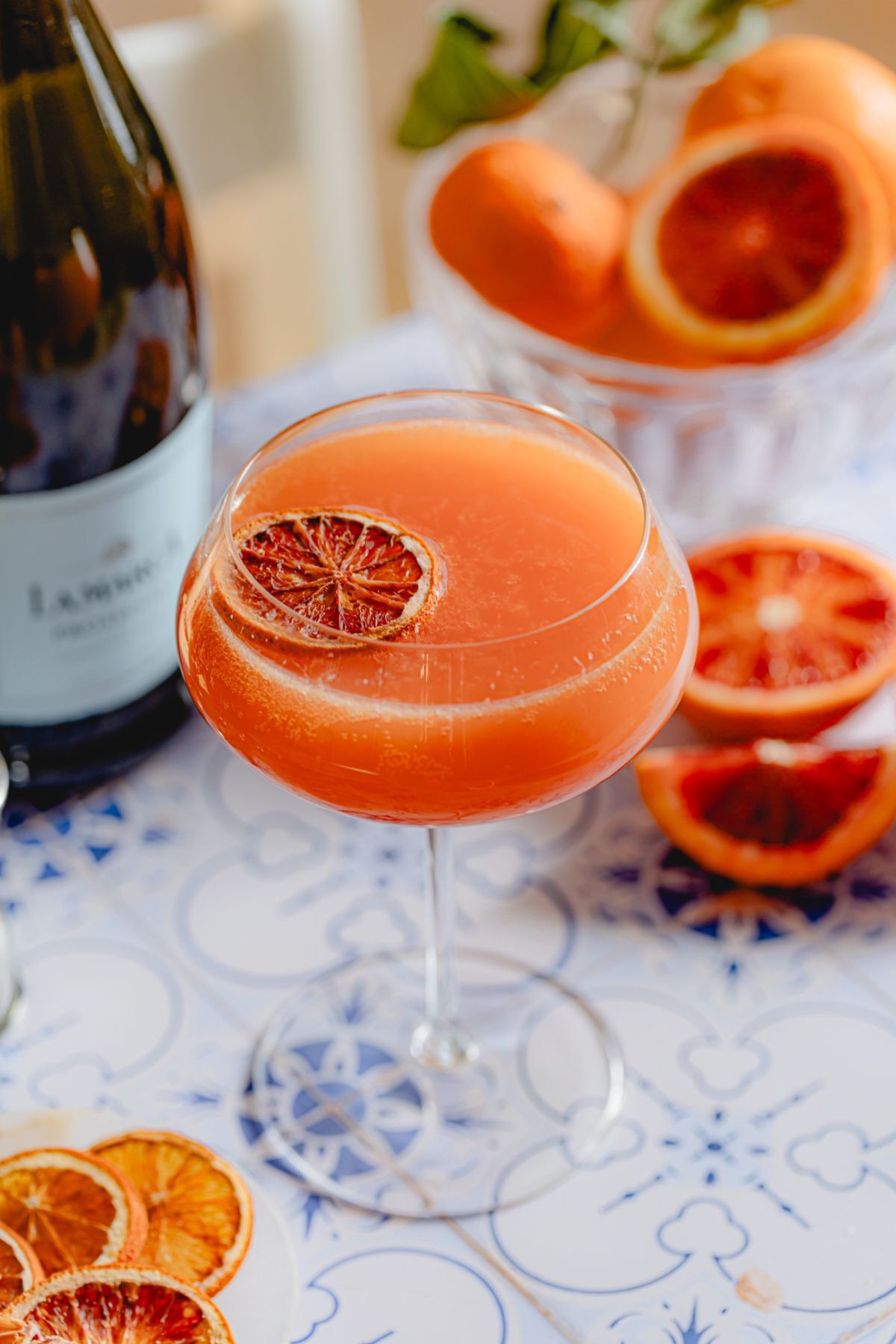Blood Orange 75 Prosecco cocktail garnished with a dried citrus wheel, served alongside fresh blood orange slices.