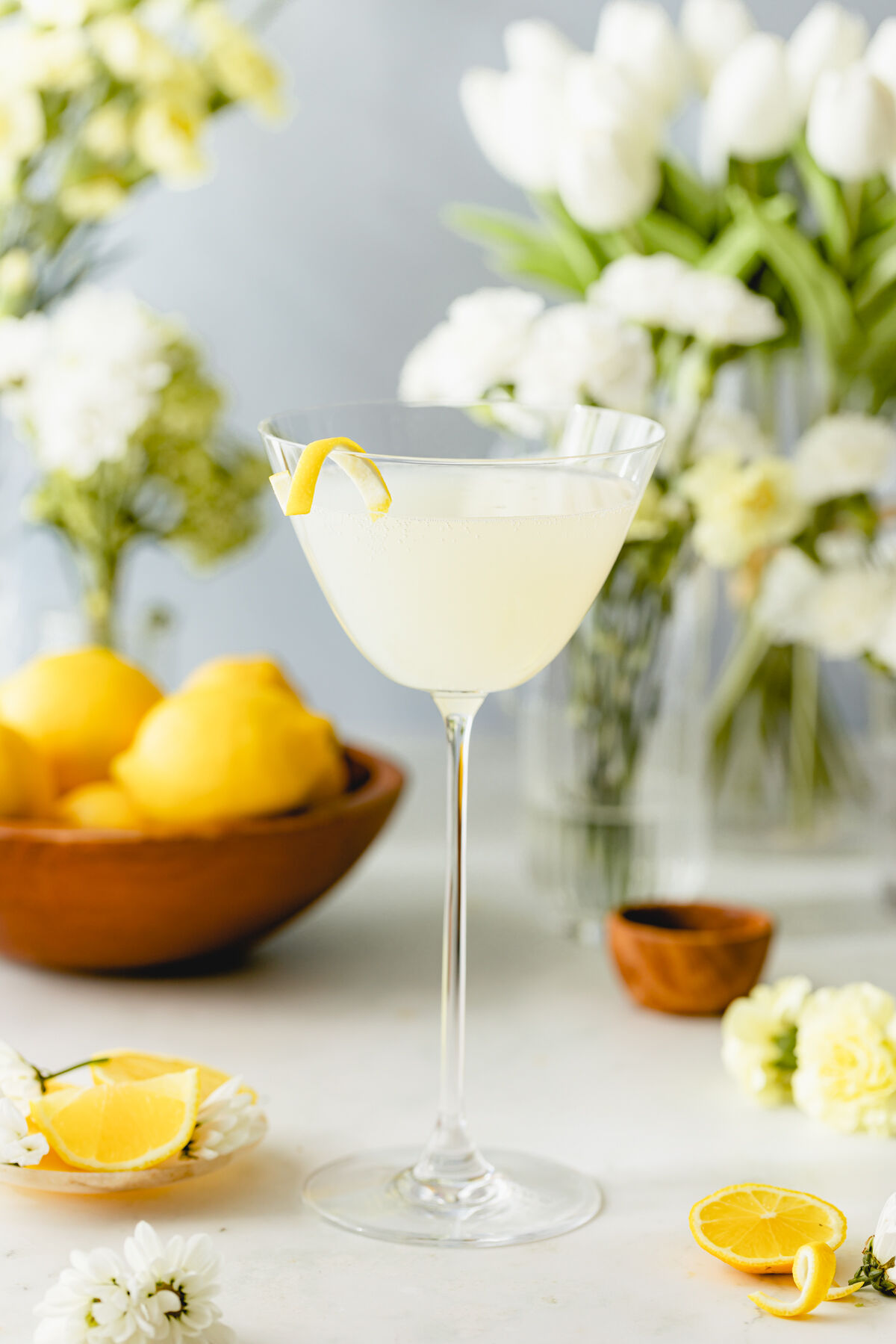 Lemon Bliss Prosecco cocktail served in a coupe glass with a lemon twist garnish, styled with fresh lemons and white flowers.